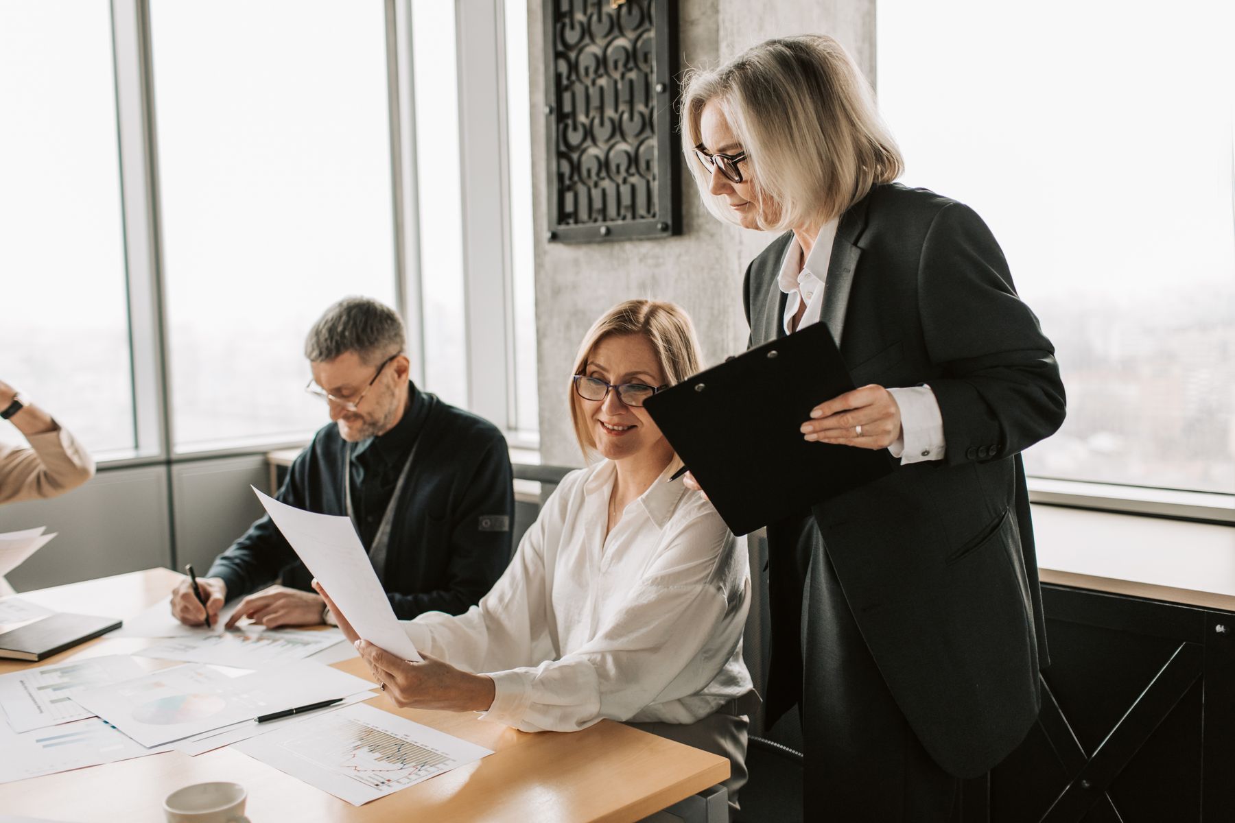 Colleagues reviewing printed reports at a meeting table, with one taking notes and another holding a clipboard